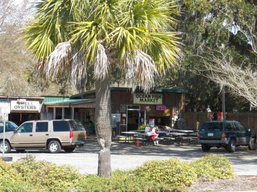 A seafood market with a wooden exterior, surrounded by palm trees and parked cars, featuring outdoor seating.