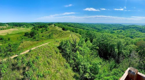 A panoramic view of lush green hills and a winding trail under a clear blue sky.