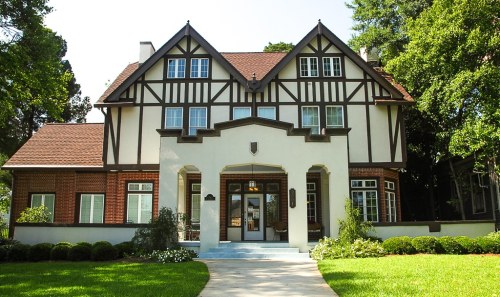 A large, two-story Tudor-style house with a brick and white exterior, surrounded by green lawns and trees.