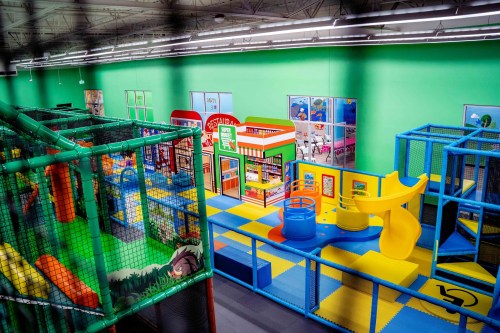 Colorful indoor playground with slides, climbing structures, and play areas, surrounded by green walls.