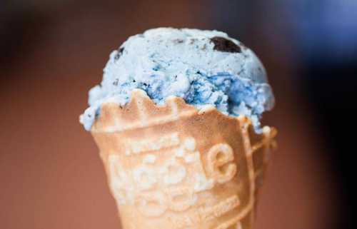 A close-up of a blue ice cream scoop in a waffle cone, featuring chocolate cookie pieces.