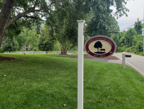 Sign for Maple Hollow Farm, established in 2012, set in a green landscape with trees and a white fence.