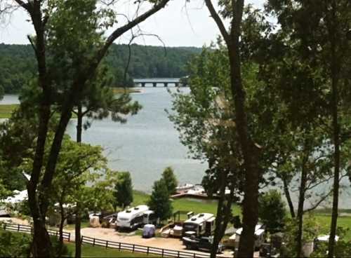 A serene lake view with trees, a bridge in the distance, and RVs parked along the shore.