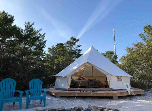 A white tent on a wooden platform surrounded by trees, with two blue chairs in front and a clear blue sky above.