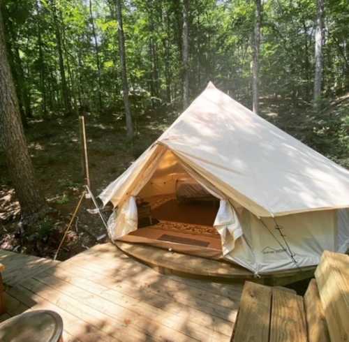 A glamping tent on a wooden deck surrounded by trees in a serene forest setting.