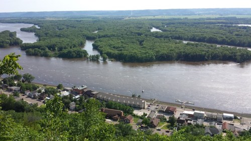 Aerial view of a river winding through lush green trees, with a small town along the riverbank in the foreground.