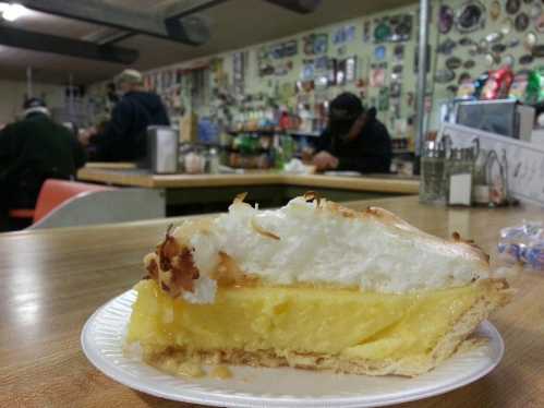 A slice of lemon meringue pie on a plate, with a cozy diner setting in the background.