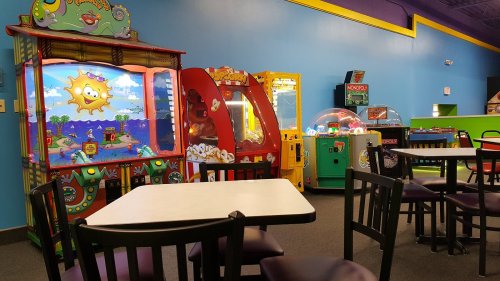 Colorful arcade games in a bright room with empty tables and chairs.