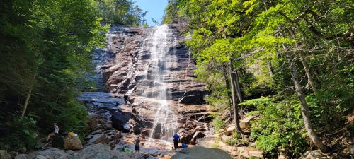 A scenic waterfall cascading down rocky cliffs, surrounded by lush green trees and people enjoying the view below.