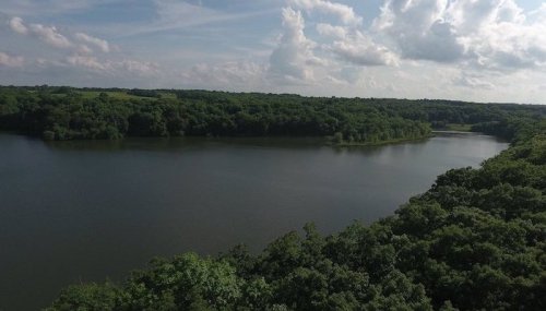 A serene lake surrounded by lush greenery under a partly cloudy sky.