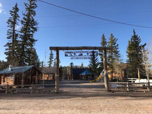 A rustic entrance sign welcomes visitors to a cabin area surrounded by tall trees and clear blue skies.