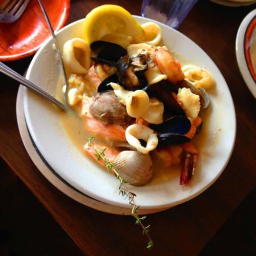 A plate of seafood featuring shrimp, clams, mussels, and calamari, garnished with lemon and herbs.