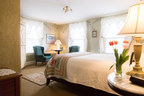 Cozy bedroom with a large bed, floral decor, a lamp, and a vase of tulips on a table by a window.
