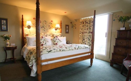 Cozy bedroom with a four-poster bed, floral bedding, and natural light from a large window.