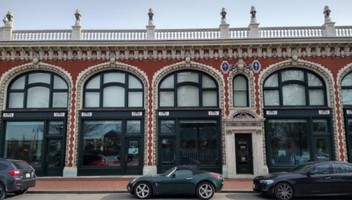 Historic brick building with arched windows and decorative details, featuring a green sports car parked in front.