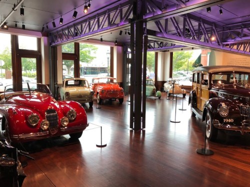 A spacious car museum featuring vintage vehicles, including classic cars from various eras, displayed on wooden flooring.