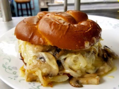 A close-up of a cheesy mushroom and onion sandwich on a soft, golden-brown bun, served on a white plate.