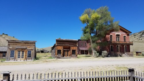 A historic ghost town with wooden buildings and a red brick structure under a clear blue sky.