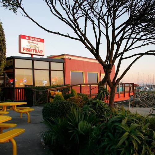 A waterfront restaurant named "Fishttrap" with outdoor seating and a view of boats in the background.