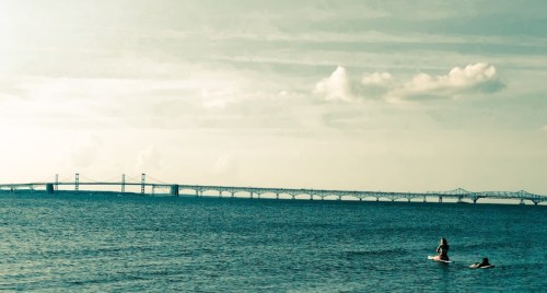 A serene view of a bridge over calm waters, with a person paddleboarding in the foreground.