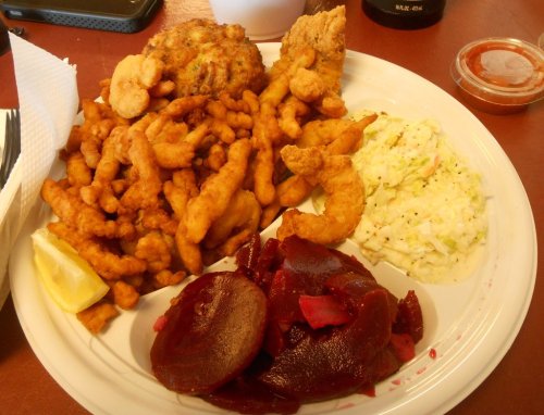 A plate of fried seafood, including shrimp and fish, with coleslaw, beets, and a lemon wedge on the side.
