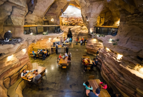 A spacious, cave-like restaurant with rock formations, tables, and diners enjoying their meals in a unique setting.