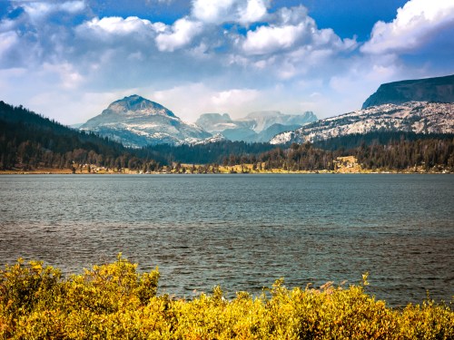 A serene lake surrounded by mountains and lush greenery under a partly cloudy sky.
