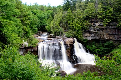 A serene waterfall cascades over rocks, surrounded by lush green trees and a tranquil river.