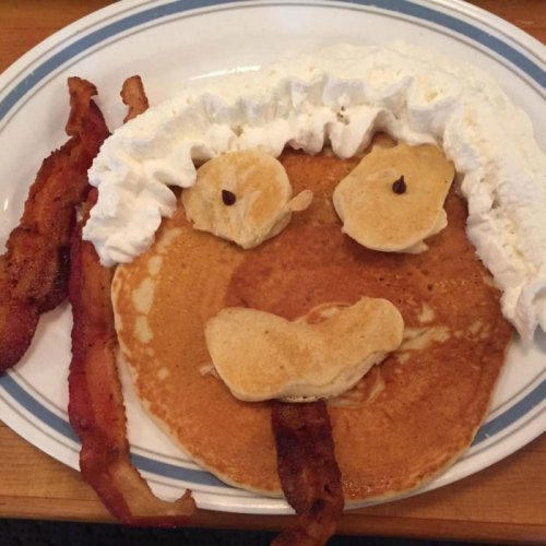 A plate of pancakes arranged to look like a smiling face, with bacon and whipped cream as features.