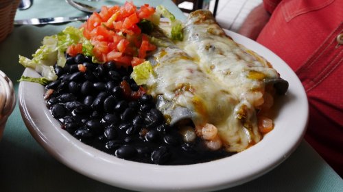 A plate of enchiladas topped with melted cheese, served with black beans, lettuce, and diced tomatoes.