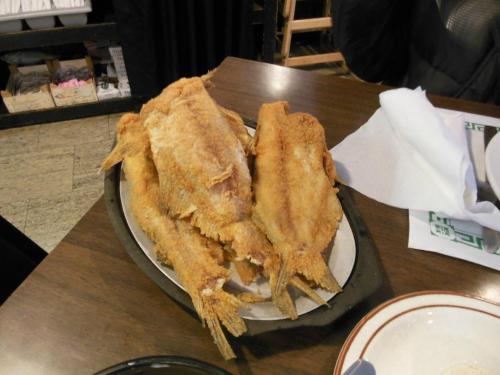 A platter of golden-brown fried fish served on a metal tray, placed on a wooden table.