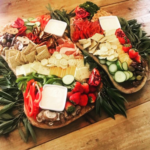 A colorful charcuterie board featuring meats, cheeses, fruits, and crackers arranged on a wooden table.