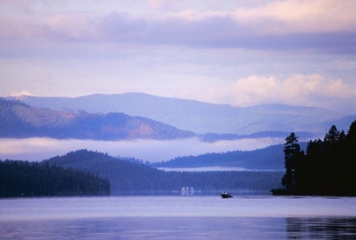 A serene lake surrounded by misty mountains and trees, with a small boat gliding across the water.
