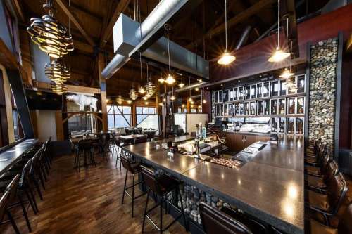 Modern restaurant interior featuring a bar, wooden beams, and large windows with a view. Cozy and inviting atmosphere.