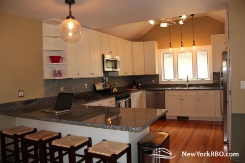 Modern kitchen with granite countertops, white cabinets, and a large window, featuring a laptop on the island.