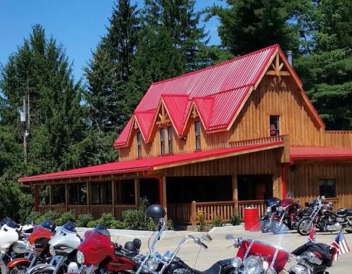 A wooden building with a red roof surrounded by trees, with several motorcycles parked in front.