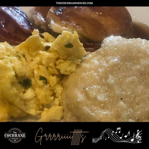 A plate of scrambled eggs, grits, and sliced sausage, served with a biscuit and gravy.
