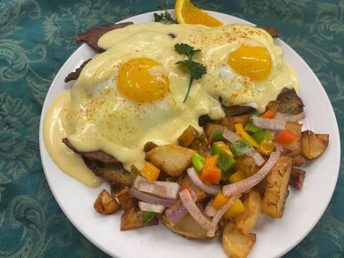 A plate of eggs topped with creamy sauce, served with golden potatoes and a colorful vegetable medley, garnished with orange.