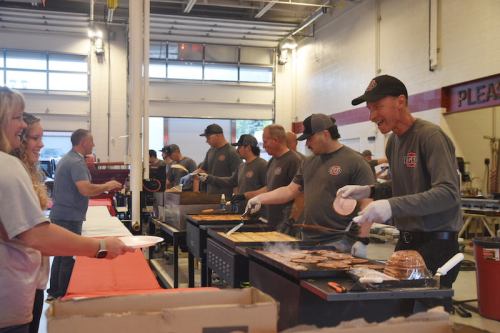 A group of people cooking and serving food at a community event, with attendees receiving plates of food.