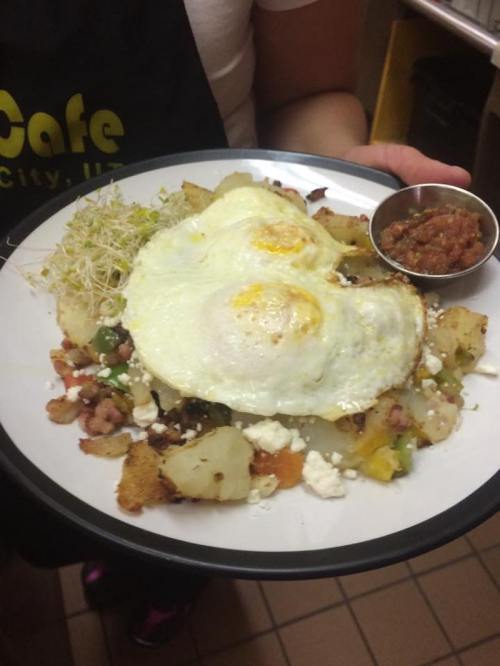 A plate of breakfast featuring two fried eggs, seasoned potatoes, vegetables, sprouts, and a side of salsa.