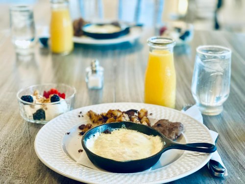 A breakfast table featuring a skillet with eggs, potatoes, yogurt with berries, and drinks.