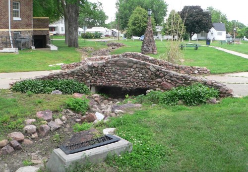A small stone bridge over a dry creek, surrounded by grass and trees in a park setting.