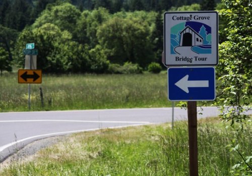 Sign for the Cottage Grove Bridge Tour with directional arrows, set against a green landscape and road.