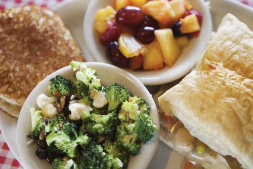 A plate with pancakes, a fruit salad, a broccoli salad, and a pastry filled with chicken and vegetables.