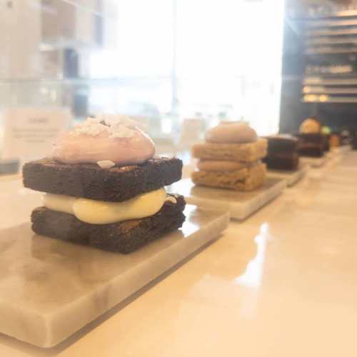 A display of assorted desserts, including brownies with frosting and layered treats on marble trays.