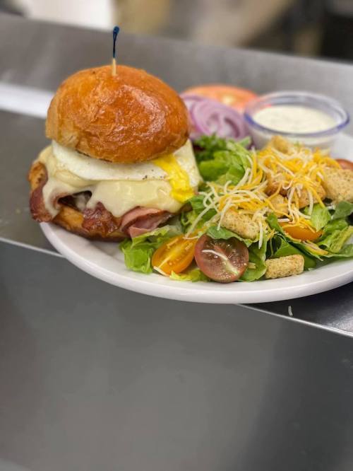 A delicious burger with bacon, cheese, and a fried egg, served with a fresh salad and dressing on the side.