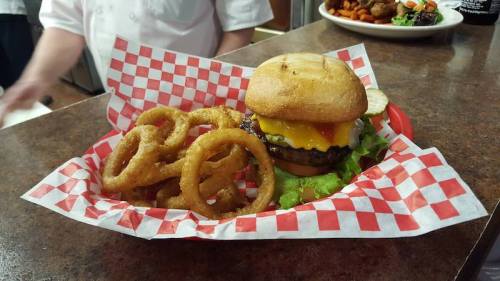 A juicy cheeseburger with lettuce and pickles, served with crispy onion rings in a red and white checkered basket.