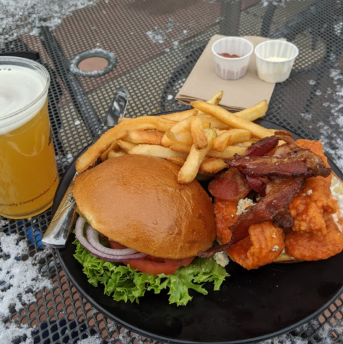 A plate with a burger, fries, and chicken tenders, alongside a glass of beer on a table.