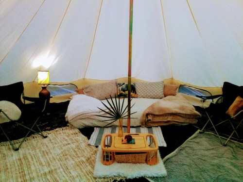 Cozy interior of a tent with cushions, blankets, a small table, and a lamp, creating a warm, inviting atmosphere.