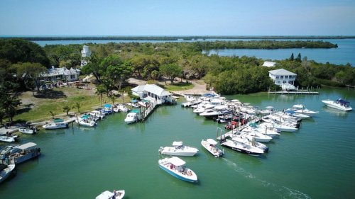 Aerial view of a marina with several boats docked, surrounded by lush greenery and calm waters.